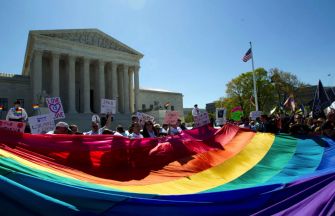 Demonstrators holding a large rainbow flag in front of the U.S. Supreme Court, advocating for LGBTQ+ rights.