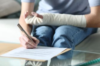 A person with a bandaged hand writing on a document while seated.