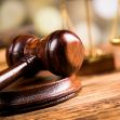 Image of a wooden gavel resting on a bench with a blurred background featuring justice scales. Image of a wooden gavel resting on a bench with a blurred background featuring justice scales.
