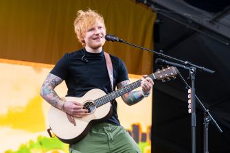 Ed Sheeran performing on stage with his guitar.