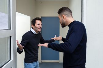 Two men appear to be in a heated argument in a doorway, gesturing expressively.
