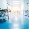 A hospital corridor with a medical stretcher in the foreground and healthcare workers in the background. A hospital corridor with a medical stretcher in the foreground and healthcare workers in the background.