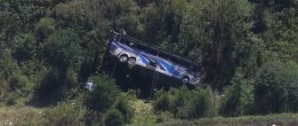 Aerial view of a blue bus that has overturned and is positioned against trees in a ravine following a crash in upstate New York.