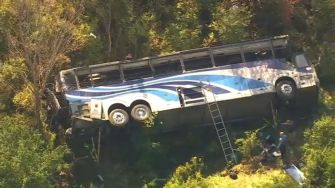 Aerial view of a charter bus that overturned at the edge of a ravine, with rescue personnel on the scene.