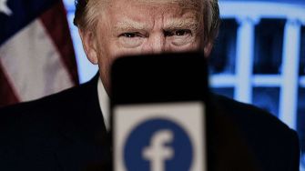 Close-up of Donald Trump with a smartphone displaying the Facebook logo in the foreground.