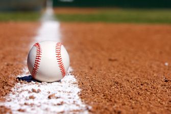 A baseball sits on the edge of a dirt infield, with a chalk line in the background.