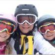 A woman and her two daughters, all wearing ski gear and helmets, smiling for a ski selfie. A woman and her two daughters, all wearing ski gear and helmets, smiling for a ski selfie.