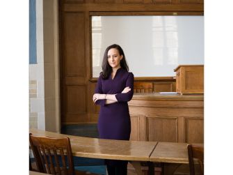 A law professor standing in a courtroom setting with arms crossed, wearing a purple dress.