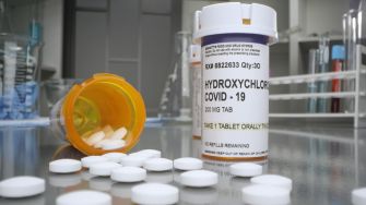 A prescription bottle for hydroxychloroquine labeled for COVID-19 treatment, with pills spilled around it on a counter.
