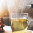 A person using a dropper to add liquid to a glass cup, possibly containing herbal tea or a supplement. A person using a dropper to add liquid to a glass cup, possibly containing herbal tea or a supplement.