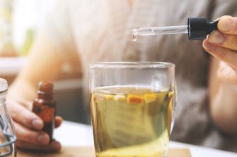 A person using a dropper to add liquid to a glass cup, possibly containing herbal tea or a supplement.