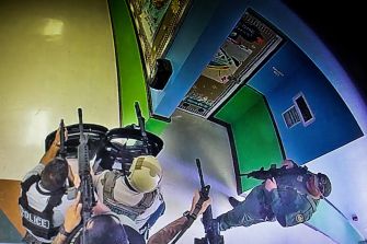 Surveillance footage showing law enforcement officers armed and gathered outside a classroom door during a school shooting incident.
