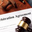 A gavel and an arbitration agreement document placed on a wooden surface. A gavel and an arbitration agreement document placed on a wooden surface.