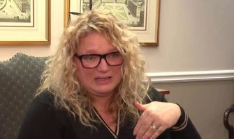 A woman with curly hair and glasses looks emotional while discussing a serious issue regarding her daughter’s safety at school.