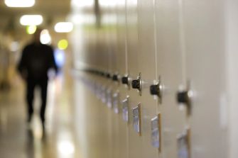 A corridor of school lockers with an out-of-focus figure walking in the background.