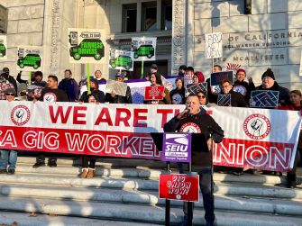 Demonstrators rallying for gig worker rights, holding signs and banners in front of a government building.