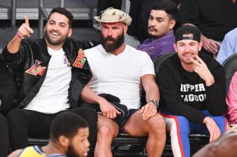 A group of men seated together at an event, smiling and gesturing, with one man in the center wearing a cowboy hat and casual attire.