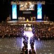 An aerial view of a graduation ceremony in a large venue, with graduates seated and a stage in the background. An aerial view of a graduation ceremony in a large venue, with graduates seated and a stage in the background.