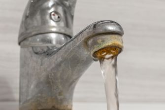 A close-up of a kitchen faucet with water flowing and visible mineral buildup and corrosion around the spout.