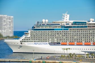 A cruise ship named Celebrity Reflection docked at a port with a clear blue sky and water in the background.