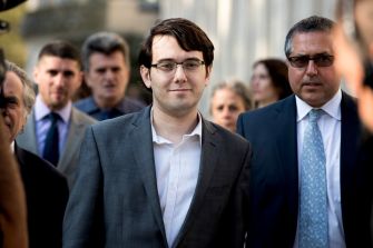Image of Martin Shkreli surrounded by individuals as he leaves a courthouse.
