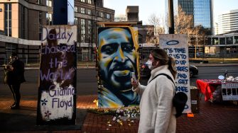 A woman walks past a mural of George Floyd, surrounded by memorial items and messages honoring his legacy.
