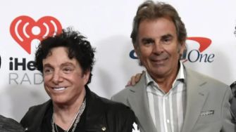 Two members of the rock band Journey posing at an event, with one member wearing a black jacket and the other in a light-colored suit.