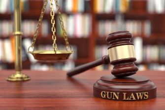 A gavel and scale symbolizing gun laws on a wooden surface, with a blurred background of bookshelves.