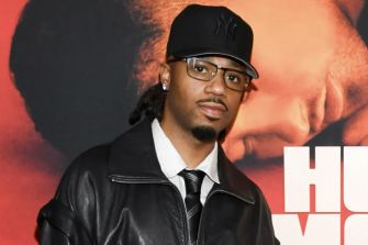 Metro Boomin at an event, wearing a black leather jacket and glasses.