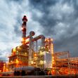 An industrial facility with pipes and smokestacks illuminated against a dramatic cloudy sky. An industrial facility with pipes and smokestacks illuminated against a dramatic cloudy sky.