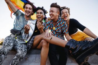 A group of four diverse individuals joyfully celebrating with a rainbow flag, showcasing pride and solidarity in the LGBTQ community.