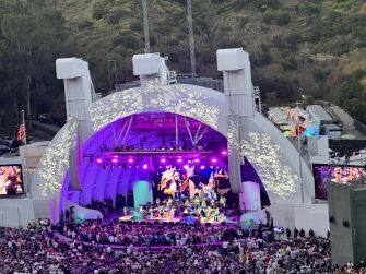 A vibrant concert scene at an amphitheater, featuring a colorful stage with performers and a large audience.