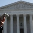 A person holding a cell phone in front of the U.S. Supreme Court building. A person holding a cell phone in front of the U.S. Supreme Court building.
