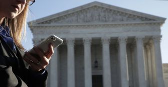 A person holding a cell phone in front of the U.S. Supreme Court building.