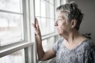 A senior woman looking thoughtfully out of a window.