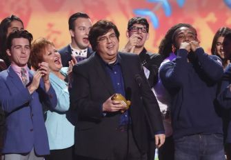 A group of people, including a man holding an award, on stage celebrating at a televised event.