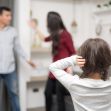 A young child covers her ears while two adults argue in the background, illustrating the impacts of domestic violence on family dynamics. A young child covers her ears while two adults argue in the background, illustrating the impacts of domestic violence on family dynamics.