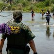 A police officer watches as migrants cross a river near the Texas-Mexico border. A police officer watches as migrants cross a river near the Texas-Mexico border.