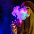 A person exhaling colorful vapor from a vaping device in a dark setting. A person exhaling colorful vapor from a vaping device in a dark setting.