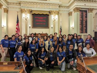 Group of students and advocates wearing blue shirts posing in a California legislative chamber.
