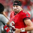 Baker Mayfield on the field, holding a football helmet while wearing a Tampa Bay Buccaneers uniform. Baker Mayfield on the field, holding a football helmet while wearing a Tampa Bay Buccaneers uniform.
