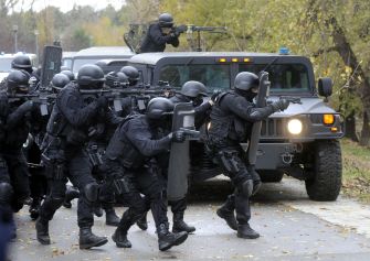 A SWAT team in tactical gear moving towards a vehicle during an operation.