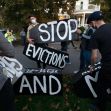 A group of protesters holding signs that read "STOP EVICTIONS AND" during a demonstration. A group of protesters holding signs that read "STOP EVICTIONS AND" during a demonstration.