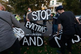 A group of protesters holding signs that read "STOP EVICTIONS AND" during a demonstration.