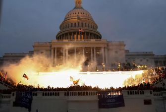 Crowds gather outside the Capitol building as smoke rises during the January 6 attack.