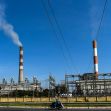 Industrial smokestacks emitting smoke under a clear blue sky, with power lines in the foreground. Industrial smokestacks emitting smoke under a clear blue sky, with power lines in the foreground.