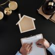 A person signing a document with a wooden house model and legal scales in the background. A person signing a document with a wooden house model and legal scales in the background.