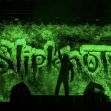 Silhouette of a musician performing on stage with a backdrop displaying the "Slipknot" logo in green lights. Silhouette of a musician performing on stage with a backdrop displaying the "Slipknot" logo in green lights.