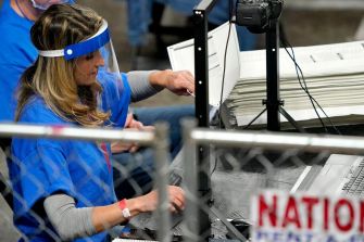 A person in a blue shirt processes ballots at a voting facility during an election audit.