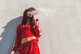 A person in a red outfit exhaling vapor against a white wall.